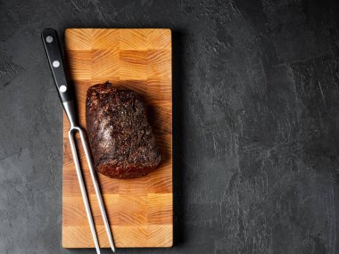 Grilled juicy beef steak selected marbled meat cutting on slices on wooden desk black background with folk and knife clipart