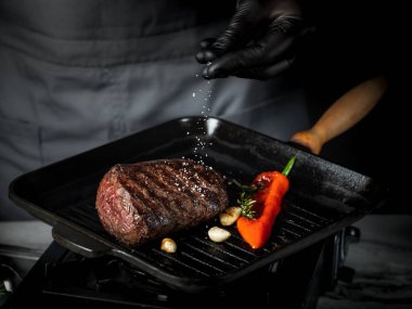 Izgarada biftek fileto pişiriyorum. Siyah arka planda tuz ve biber ve fotokopi uzay metni. Yemek tarifi konsepti