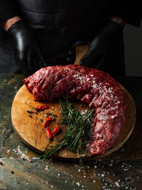 Biberli büyük bıçaklı kasapla biftek fileto eti, tuz, taş masa üzerinde otlar arka planda. Düz görünüm, genel görünüm