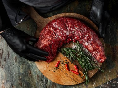 Biberli büyük bıçaklı kasapla biftek fileto eti, tuz, taş masa üzerinde otlar arka planda. Düz görünüm, genel görünüm