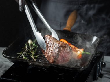 Izgarada biftek fileto pişiriyorum. Siyah arka planda tuz ve biber ve fotokopi uzay metni. Yemek tarifi konsepti