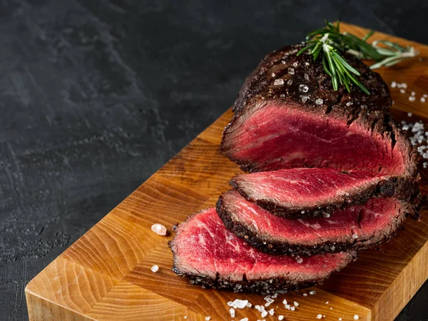 Izgara sulu biftek seçilmiş mermer et dilimler üzerinde tahta masa üzerinde siyah arka plan halk ve bıçak ile kesilmiş