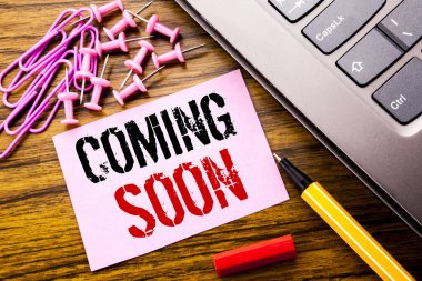 Handwritten text showing Coming Soon. Business concept for Message Future written on pink sticky note paper on the wooden background next to keyboard. With red pen. clipart