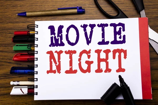 Handwriting Announcement text showing Movie Night. Business concept for Wathing Movies  Written on notebook, wooden background with office equipment like pens scissors colourful marker
