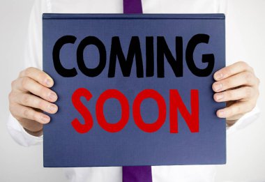 Coming Soon gösterilen metin yazma. İş kavramı altında İnşaat tarafından adam bulanık takım elbise arka planda tutarak kitap defter kağıt üzerinde yazılı için.