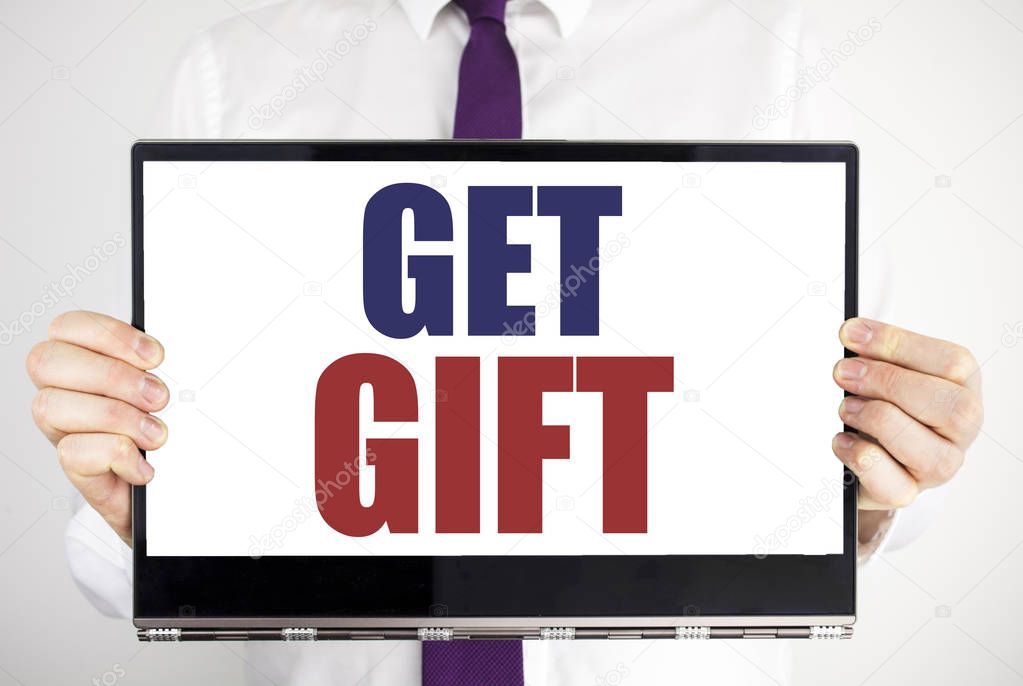 Word, writing Get Gift. Business concept for Free Shoping Coupon Written on tablet laptop holding by the man blurred background. Businessman fingers keeping the computer.