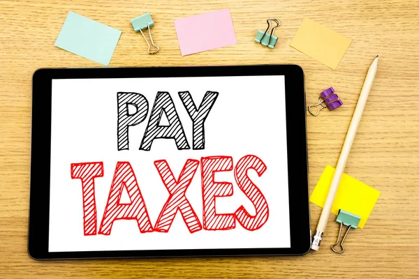 Escrevendo texto mostrando Pay Taxes. Conceito de negócio para tributação sobre a devolução Escrito em tablet laptop, fundo de madeira com nota pegajosa e caneta — Fotografia de Stock