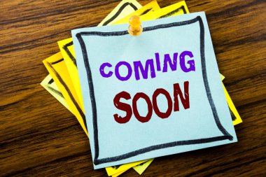 Coming Soon gösterilen metin yazma. İş kavramı altında inşaat ahşap arka plan üzerinde yapışkan not kağıt üzerinde yazılı için.