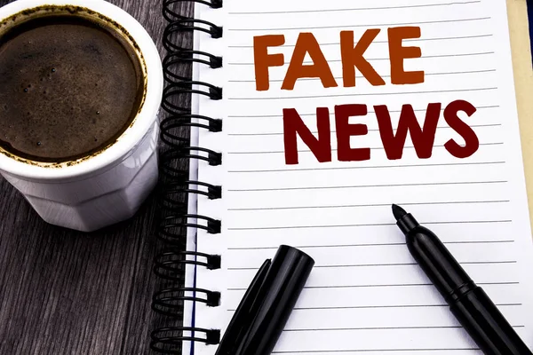 Escrevendo texto mostrando Fake News. Conceito de negócio para o jornalismo Hoax escrito em papel de nota de caderno sobre o fundo de madeira de madeira. Com café e marcador preto . — Fotografia de Stock