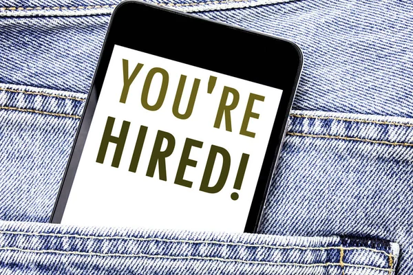 Handwriting Announcement text showing You Are Hired. Business concept for Hiring Employee Worker Written phone mobile phone, cellphone placed in the man front jeans pocket.