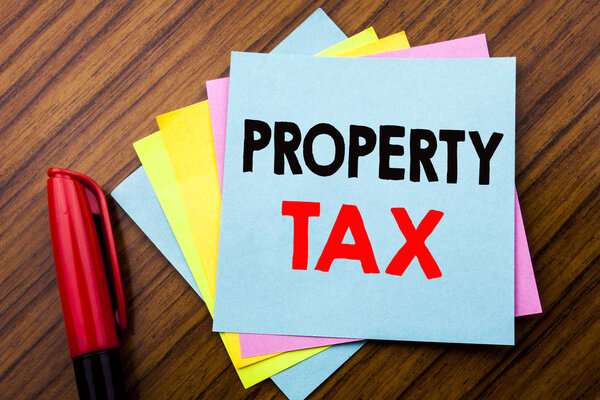 Почерк Объявление текстового налога на имущество. Концепция налогообложения доходов от недвижимости Написана на липкой бумаге с деревянным фоном с видом на космический офис с карандашным маркером
