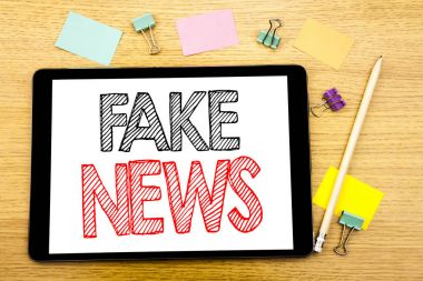 Writing text showing Fake News. Business concept for Hoax Journalism Written on tablet laptop, wooden background with sticky note and pen clipart