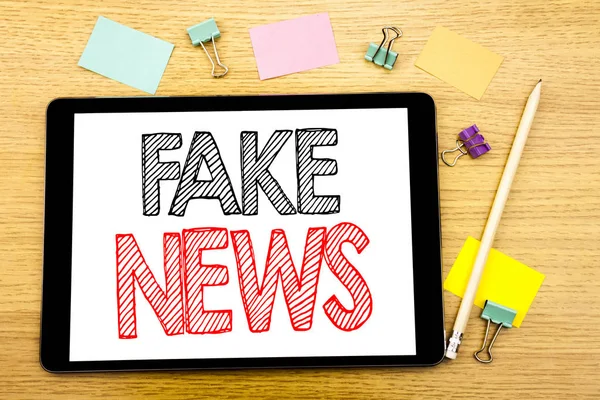 Text schreiben, der Fake News zeigt. Geschäftskonzept für Falschjournalismus auf Tablet-Laptop geschrieben, Holzgrund mit Haftnotiz und Stift — Stockfoto