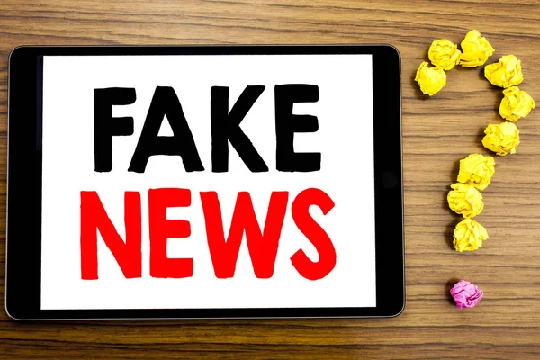 Tekst intoetsen met Fake Nieuws. Businessconcept voor Hoax journalistiek geschreven op tablet pc op de houten achtergrond met vraagteken gemaakt van gevouwen papier. — Stockfoto