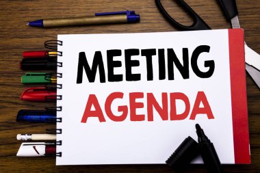 Toplantı Ajandası gösteren el yazısı metin. İş zamanlama planı yazılı üstünde defter, kalem gibi Ofis donanımı ile ahşap arka plan için iş konsepti renkli marker makas  