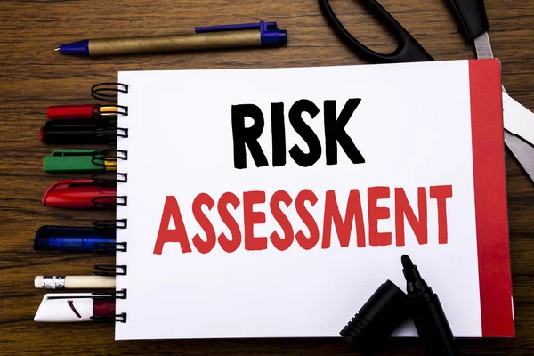 Handwritten text showing Risk Assessment. Business concept for Safety Danger Analyze Written on notebook, wooden background with office equipment like pens scissors colourful marker