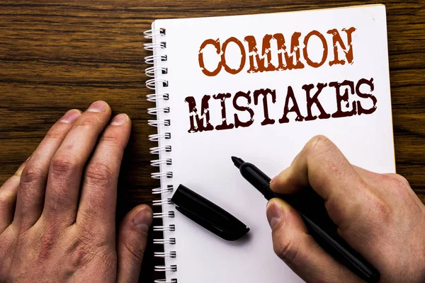 Handwritten text showing word Common Mistakes. Business concept for Common Concept Written on tablet laptop, wooden background with businessman hand, finger writing on notebook book.