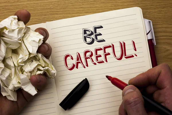Handwriting text Be Careful. Concept meaning Caution Warning Attention Notice Care Beware Safety Security written by Man on Notebook Book Holding Marker on the wooden background Pen next to it.