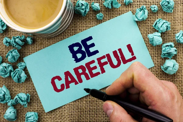 Writing note showing  Be Careful. Business photo showcasing Caution Warning Attention Notice Care Beware Safety Security written by Man Holding Pen on Sticky Note Paper the jute background Cup