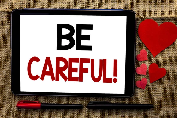 Handwriting text writing Be Careful. Concept meaning Caution Warning Attention Notice Care Beware Safety Security written on Tablet on the jute background Hearts and Pens next to it.