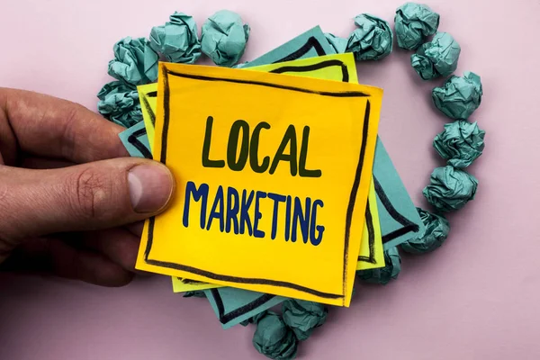 Handwriting text Local Marketing. Concept meaning Regional Advertising Commercial Locally Announcements written on Sticky Note Paper Holding by man plain background on Heart Paper Balls.
