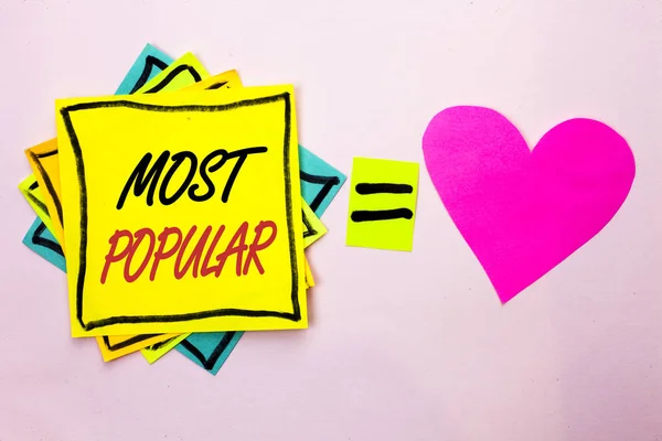 Sinal de texto mostrando Mais Popular. Foto conceitual Avaliação Top Bestseller Favorito Produto ou Artista 1st in ranking written on Yellow Sticky Note Paper on the plain background Pink Heart next to it . — Fotografia de Stock