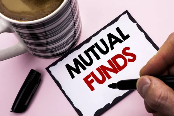Handwriting text writing Mutual Funds. Concept meaning Investment Strategy to purchase shares with other investors written by Man on Sticky Note paper holding Marker plain background Coffee Cup