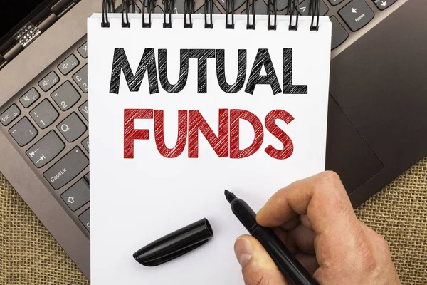 Word writing text Mutual Funds. Business concept for Investment Strategy to purchase shares with other investors written by Man Holding Pen on Notebook Book placed on Laptop with jute background