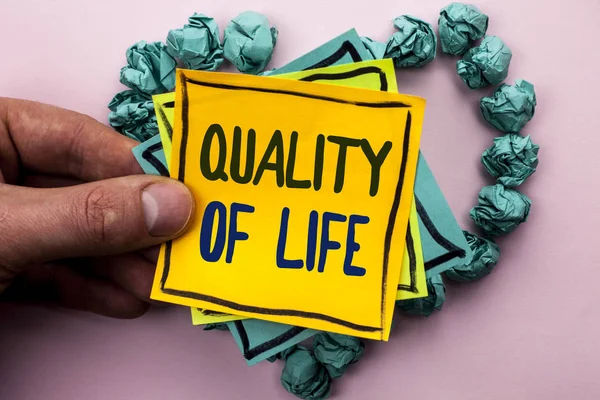 Handwriting text Quality Of Life. Concept meaning Good Lifestyle Happiness Enjoyable Moments Well-being written on Sticky Note Paper Holding by man plain background on Heart Paper Balls. — Stock Photo, Image