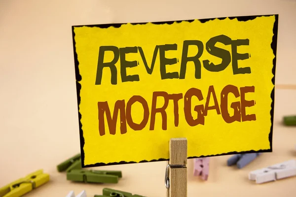 Handwriting text writing Reverse Mortgage. Concept meaning Elderly homeowner retirement option regular payment benefit written on Yellow Sticky Note Paper on the plain background Wooden Clips.