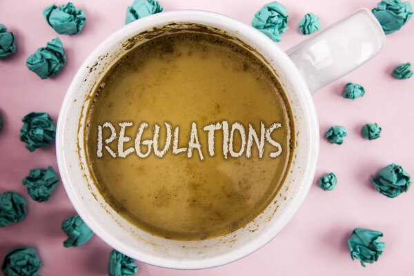 Handwriting text Regulations. Concept meaning Rules Laws Corporate Standards Policies Security Statements written on Coffee in White Cup within Crumpled Paper Balls on plain pink background.