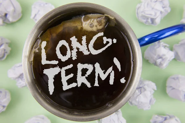 Text sign showing Long-Term Motivational Call. Conceptual photo Occurring over large period of time Future plans written on Black Tea in Cup within Crumpled Paper Balls on plain Green background. — Stock Photo, Image