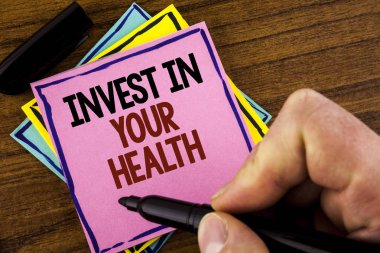 Word metin Invest sağlığınızda yazma. Kişisel Sağlık önleyici pembe yapışkan not kağıt holding marker ahşap arka plan üzerinde adam tarafından yazıldı testlerinde harcama karşılığı iş kavramı 