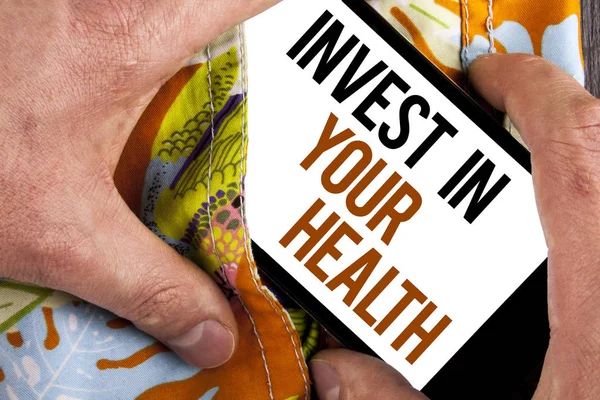 Writing note showing  Invest In Your Health. Business photo showcasing Spend money in personal healthcare Preventive Tests written on Mobile Screen holding by man on the printed background.