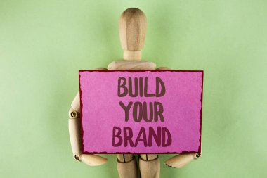 Build Your marka yazma el yazısı metin. Kendi logo sloganı Model reklam E yapışkan not kağıdı düz arka plan üzerinde tutmak ahşap Robot oyuncak tarafından yazıldı pazarlama oluşturmak anlam kavramı.