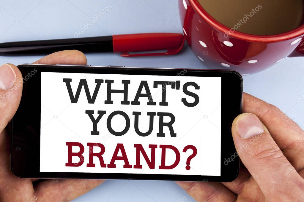 Word writing text What Is Your Brand Question. Business concept for Define Individual trademark Identify Company written Mobile Phone Screen holding by man the plain background Cup Marker