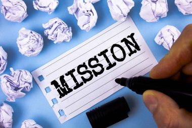 Metin misyonu yazılı kelime. Mavi arka plan kağıt topları yanında iş kavramı kurumsal hedef önemli atama iş amacı için ve odak düz kağıda not defteri adam tarafından yazıldı.