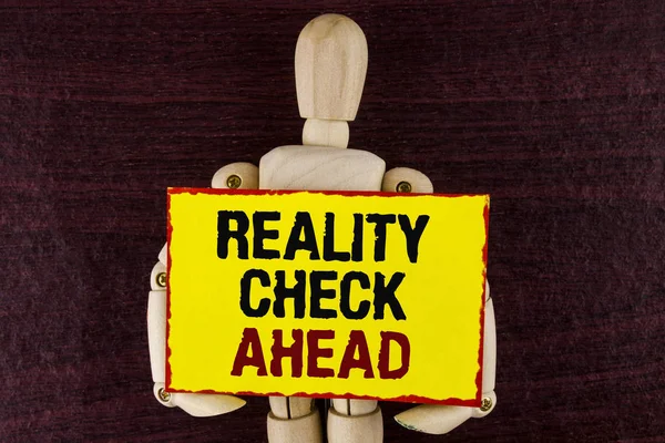 Texto de escritura de palabras Reality Check Ahead. Concepto de negocio para develar la verdad conociendo la actualidad, evite ser escéptico escrito en papel de nota adhesiva que sostiene Wooden Robot Toy sobre fondo de madera . —  Fotos de Stock