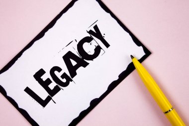 Handwriting text Legacy. Concept meaning Transmitted Received from an ancestor Money Properties given by will written on White Sticky note paper on plain Pink background Pen next to it. clipart