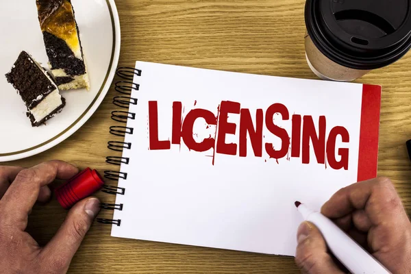 Conceptual hand writing showing Licensing. Business photo showcasing Grant a license Legally permit the use of something Allow activity written by Man on Notebook on wooden background Cake and Cup.