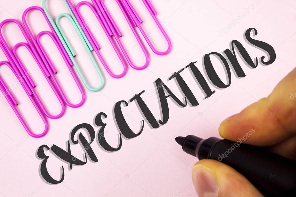 Word writing text Expectations. Business concept for Huge sales in equity market assumptions by an expert analyst written by Man holding Marker on Plain Pink background Paper Clips next to it.