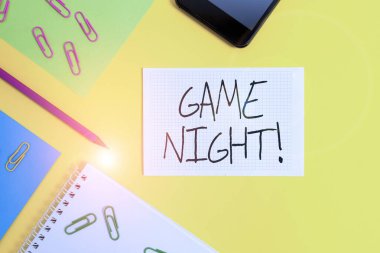 Game Night 'ı gösteren bir not yazıyorum. İş fotoğrafı gösterimi genellikle arkadaşlarıyla poker gibi yetişkin oyun tarihlerinde yapılır. Kağıt kağıtlar kare not defteri ataçları, akıllı telefon renkli arka plan..