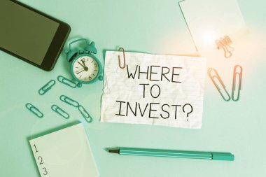Handwriting text Where To Invest Question. Concept meaning asking about where put money into financial schemes or shares Alarm clock clips notepad smartphone rubber band marker colored background.
