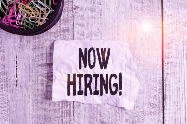 Kavramsal el yazısı Now Hiring 'i gösteriyor. İş fotoğrafı gösterimi, geleceğin çalışanları ile iş ilişkisinin değerlendirildiğini gösteriyor. Buruşuk kağıt ve karton tahta arka planın üzerine yerleştirilmiş..
