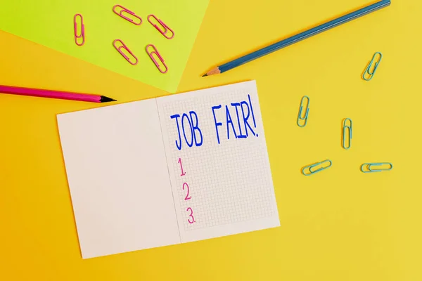 Writing note showing Job Fair. Business photo showcasing event in which employers recruiters give information to employees Blank squared notebook pencils markers paper sheet colored background.