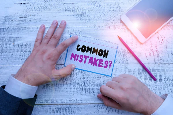 Conceptual hand writing showing Common Mistakes question. Business photo showcasing repeat act or judgement misguided or wrong Hand hold note paper near writing equipment and smartphone.