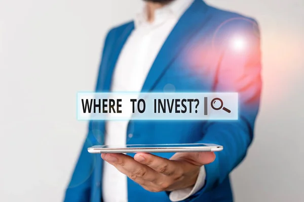 Conceptual hand writing showing Where To Invest Question. Business photo showcasing asking about where put money into financial schemes or shares Man in blue suite and white shirt holds mobile phone i — Stock Photo, Image