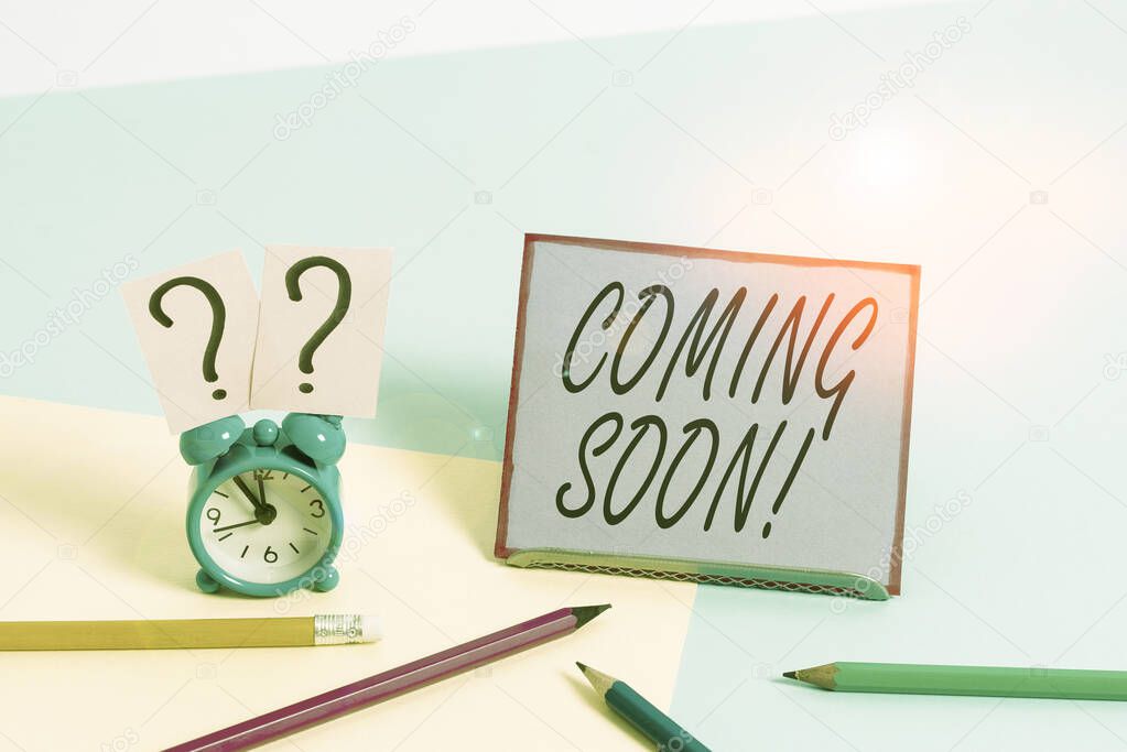 Conceptual hand writing showing Coming Soon. Business photo showcasing event or action that will happen after really short time Mini size alarm clock beside stationary on pastel backdrop.