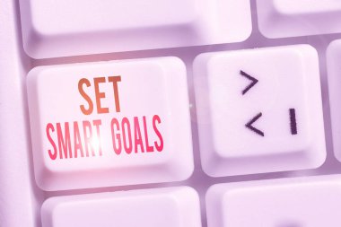 El yazısı metni Akıllı Hedefler Ayarla. Kavram, beyaz arkaplan anahtar alanının üzerinde boş not kağıdıyla hedeflerin ayarlarında rehberlik edecek kriterler vermek anlamına gelir.