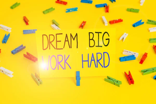 Text sign showing Dream Big Work Hard. Conceptual photo Believe in yourself and follow the dreams and goals Colored clothespin papers empty reminder yellow floor background office.